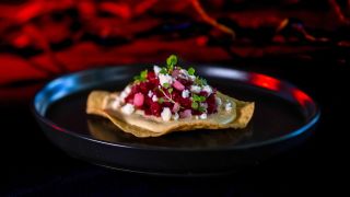 The Heart "Beet" Tostada shown plated, on a black table, in front of a red curtain, from Universal Halloween Horror Nights 33.