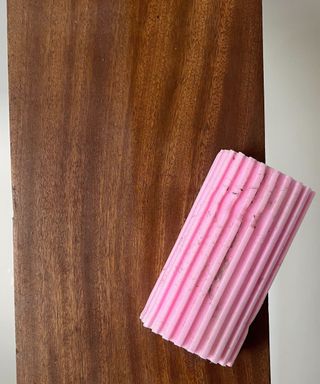 A pink scrub daddy damp duster sponge on a dusty wooden surface, one side has been cleaned and is shining, the duster is covered in dust