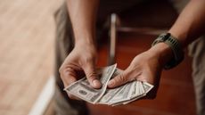 a person sits while counting one hundred dollar bills