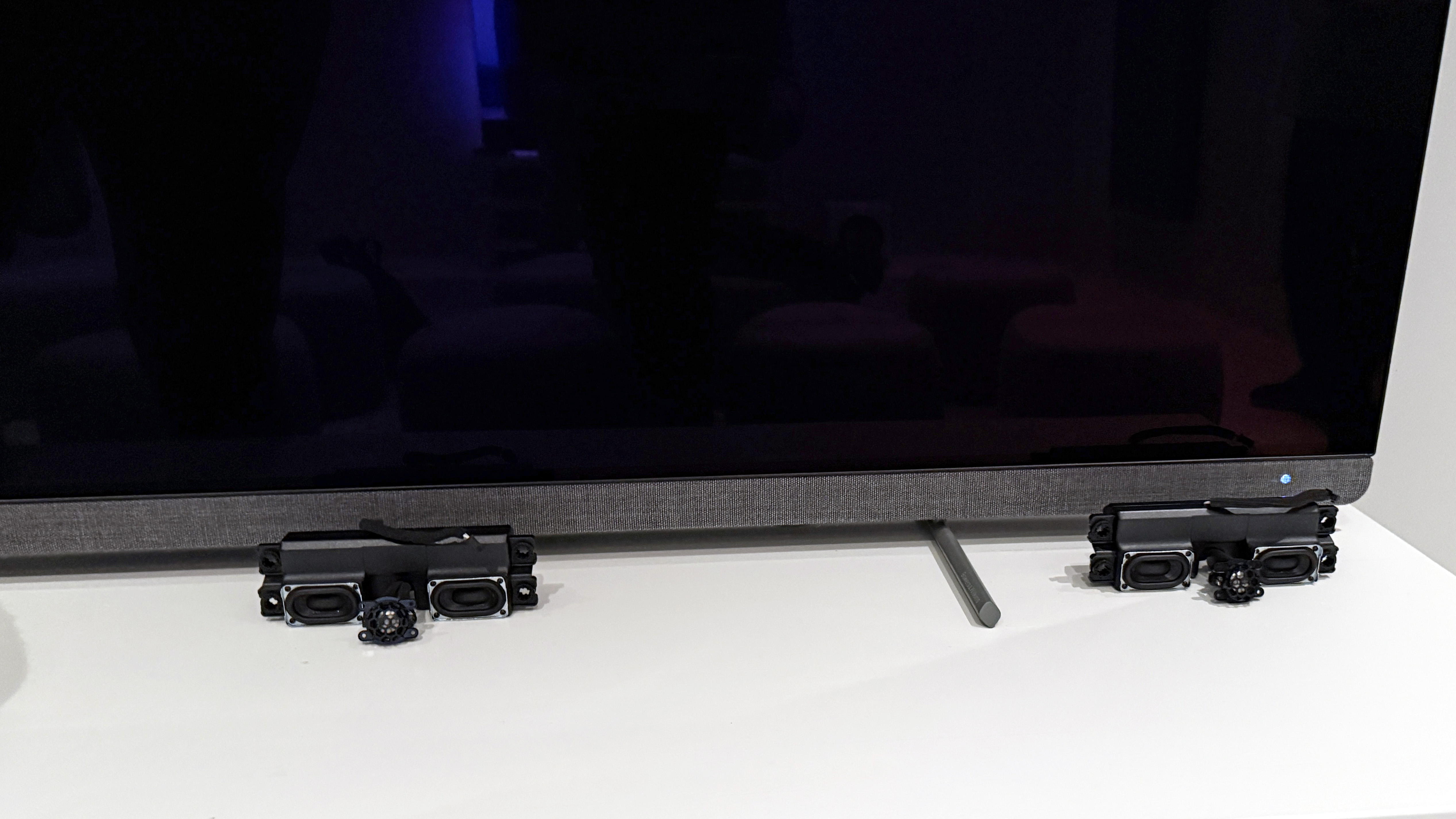 The Philips OLED+910 TV with some speaker array examples in front of it to reveal the scale