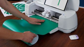 How to use a Cricut; a person feed paper and a mat into a craft machine