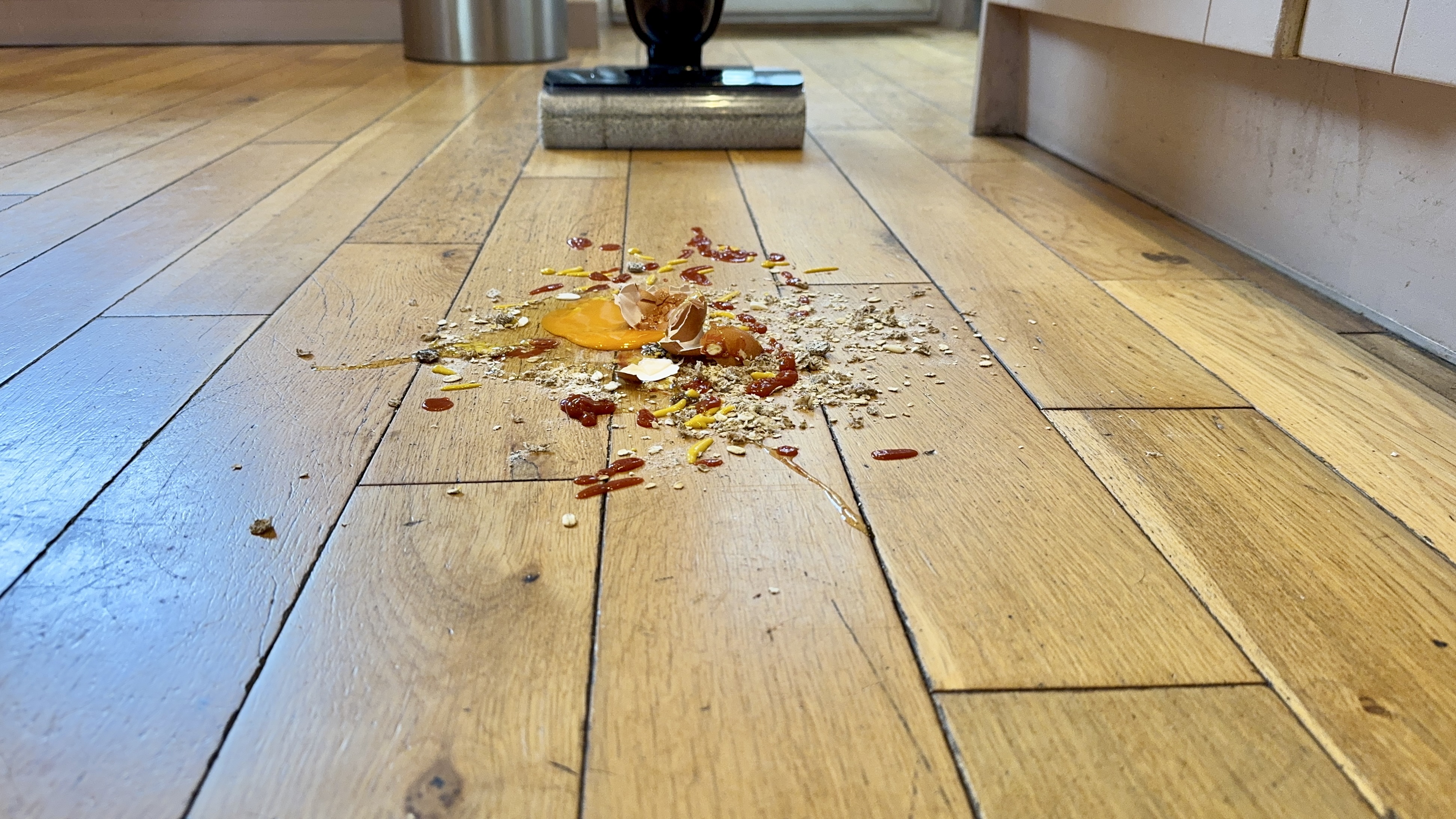 Eureka RapidWash 730 approaching a pile of oats, cracked egg, raisins and more on an engineered wood floor