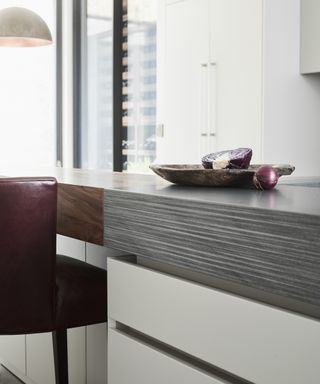 A modern kitchen island with black Vermont worktop, white cabinetry and burgundy leather chair