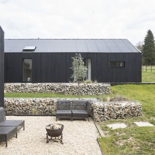 Grey outbuilding on green lawn, edged with rocks and a fire pit bowl and grey bench