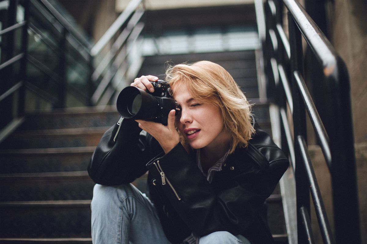 One woman, sitting outdoors on steps, holding a camera.