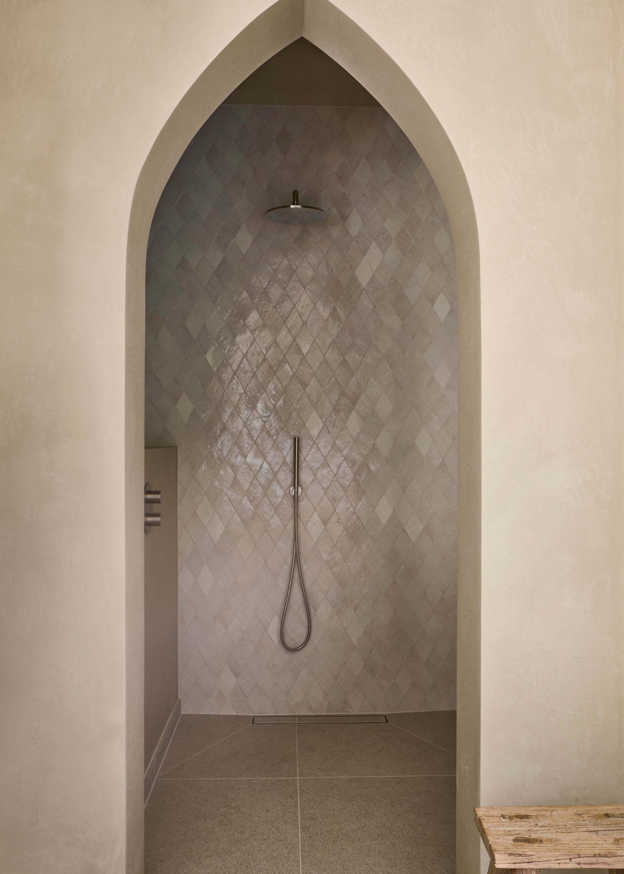 a walk in shower room with an ogival arched doorway and zellige tile covered walls