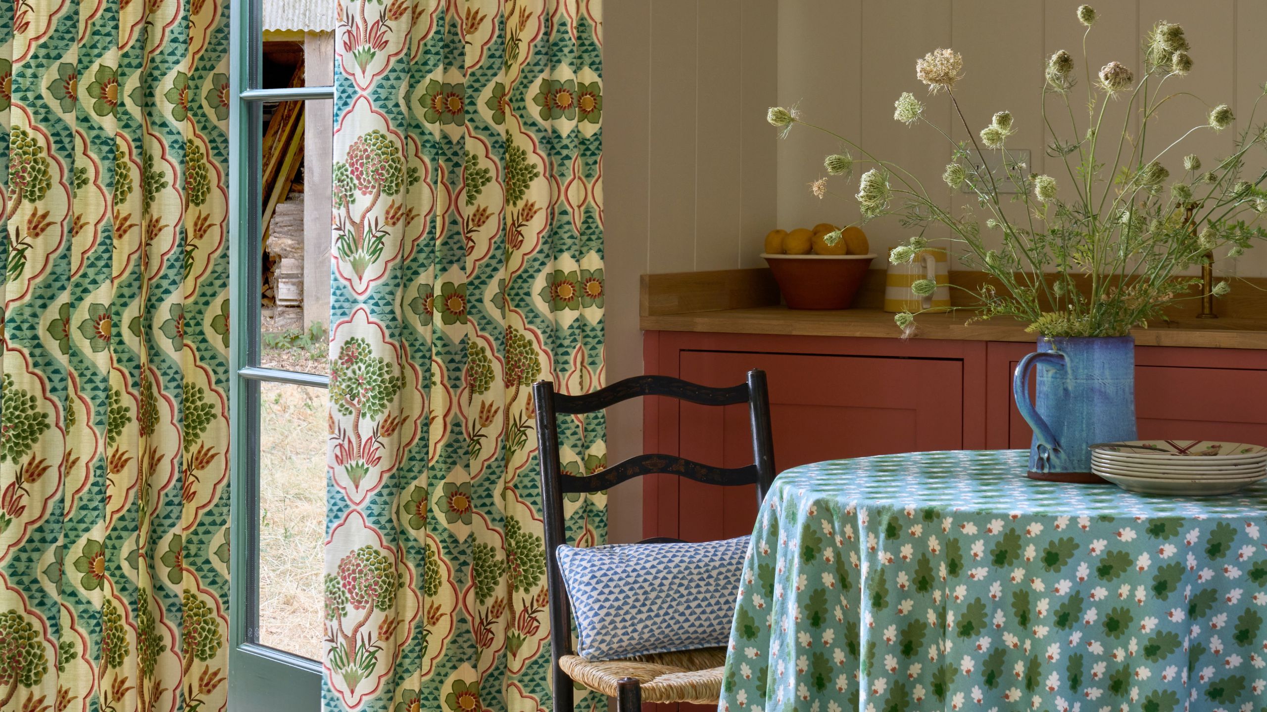Patternful dining room with circular dining table with a blue and green tablecloth and french door with a pattern curtain
