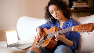 Woman practicing guitar while sitting on sofa at home