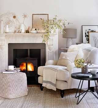 neutral living room with stone fireplace and cream armchair with pouffe