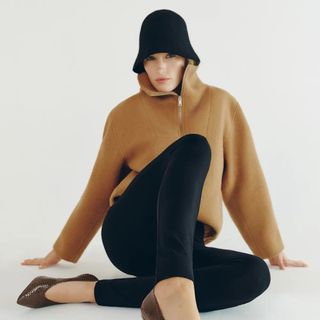 Reformation model wearing camel zip-up blouse sitting on floor