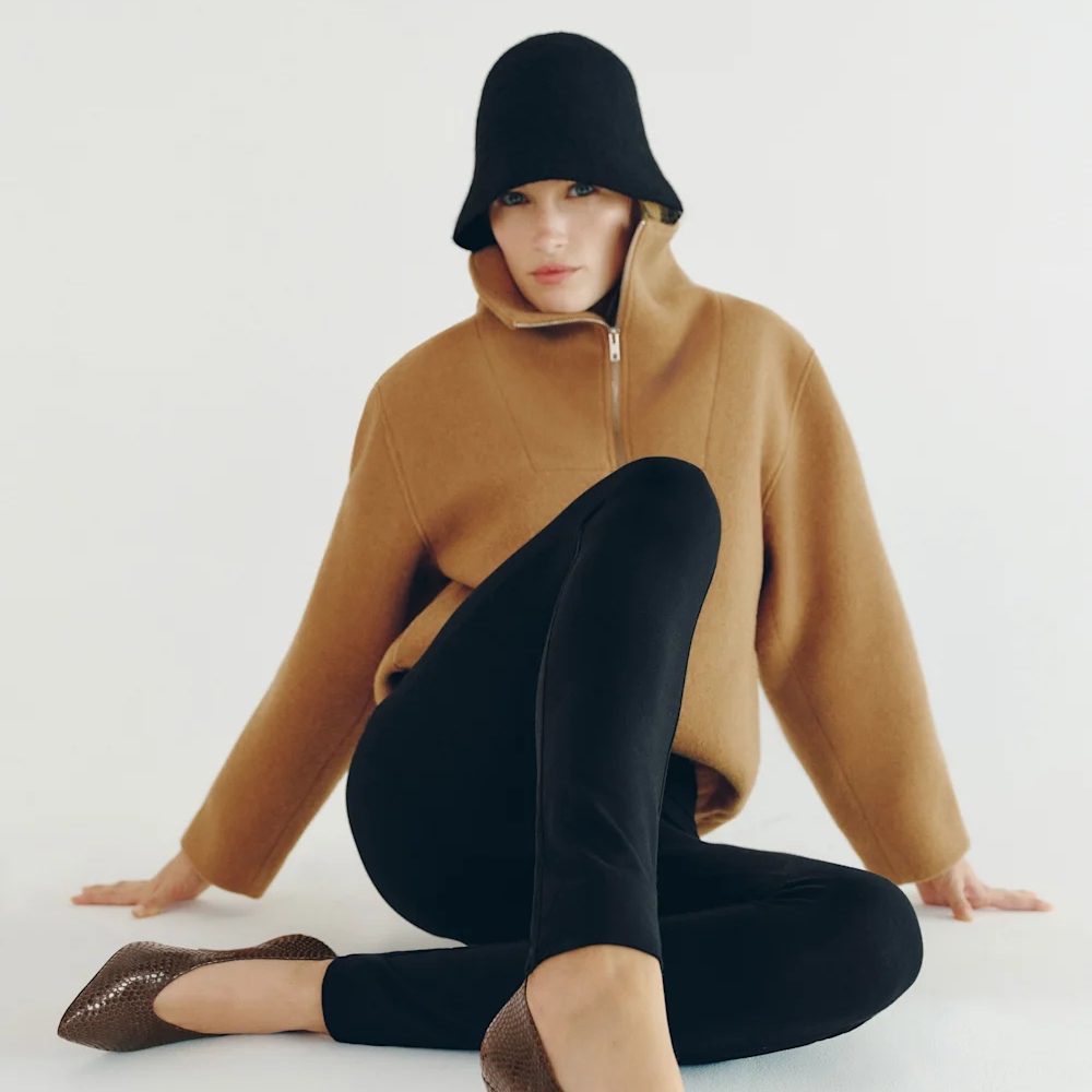 Reformation model wearing camel zip-up blouse sitting on floor