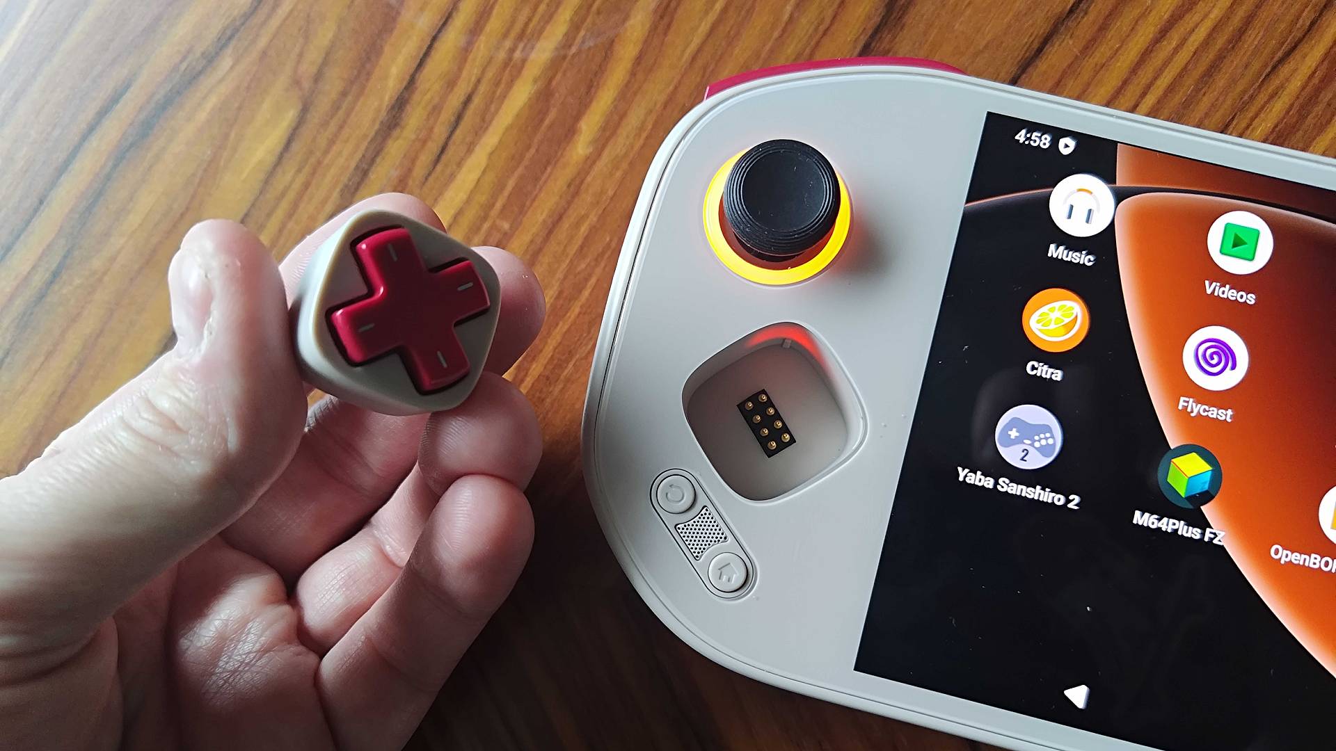 Hand holding Mangmi Pocket Maxi modular d-pad next to handheld on woodgrain table