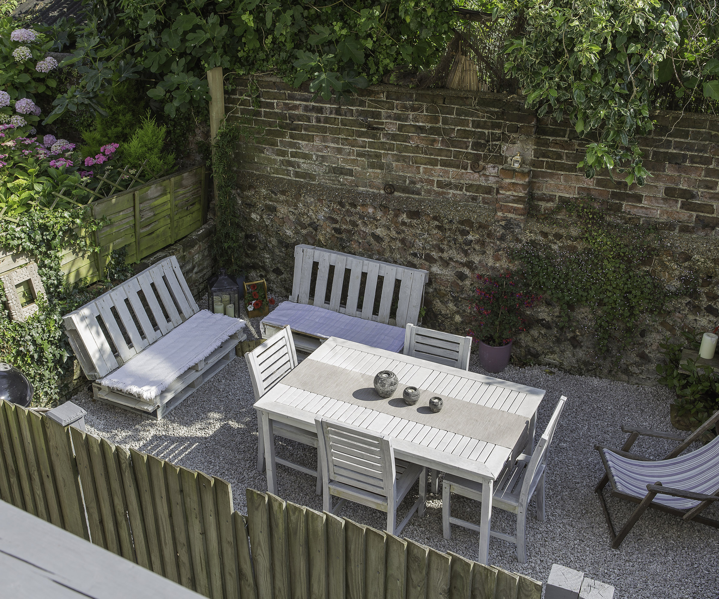 A small gravel garden with a large outdoor dining table and deck chair
