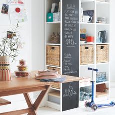 Dining area with storage shelves and baskets in the corner, blackboard panel, white walls and white painted floorboards