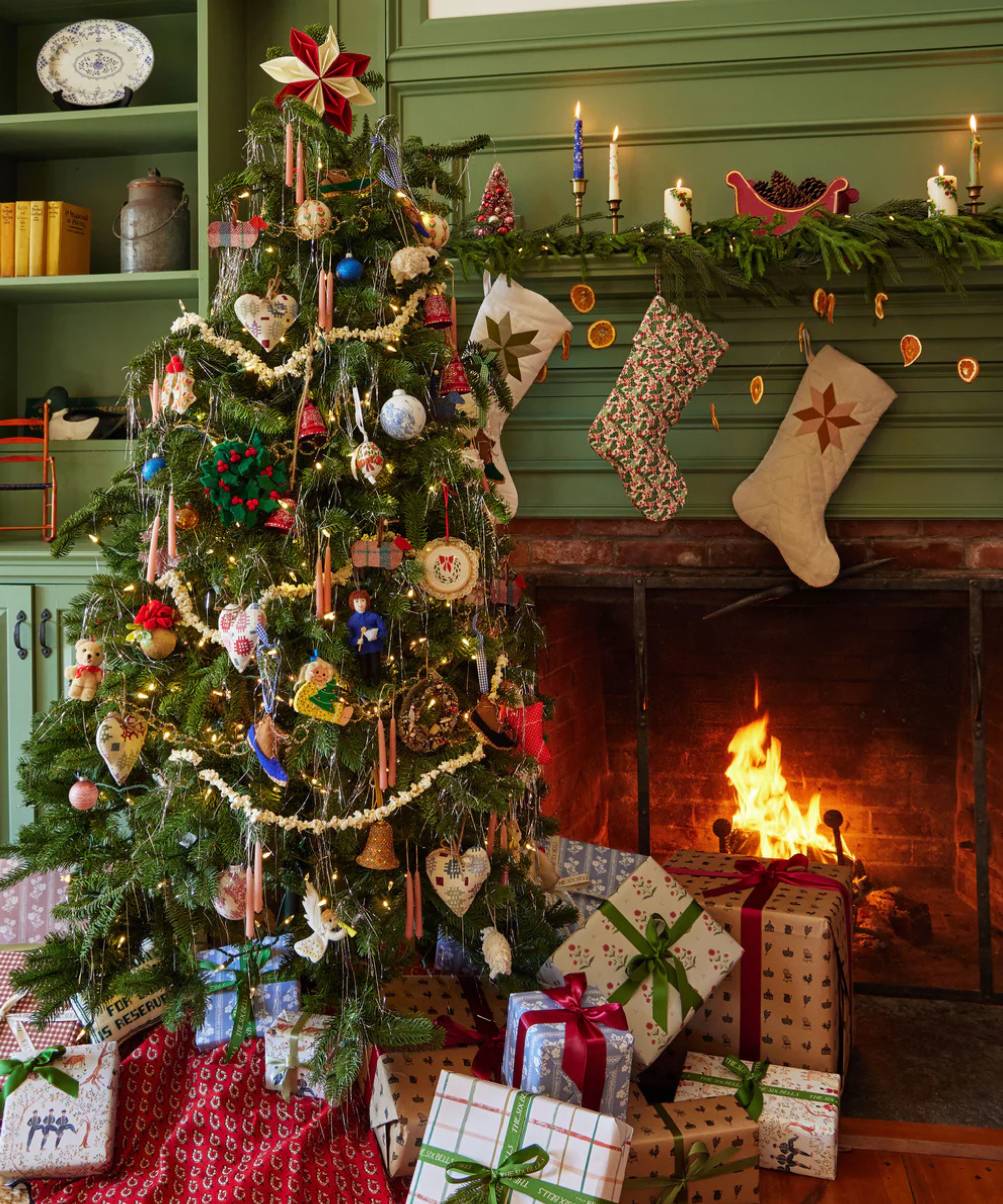 a Christmas tree festively decorated, presents beneath, a fire roaring, and stockings hanging from the mantel
