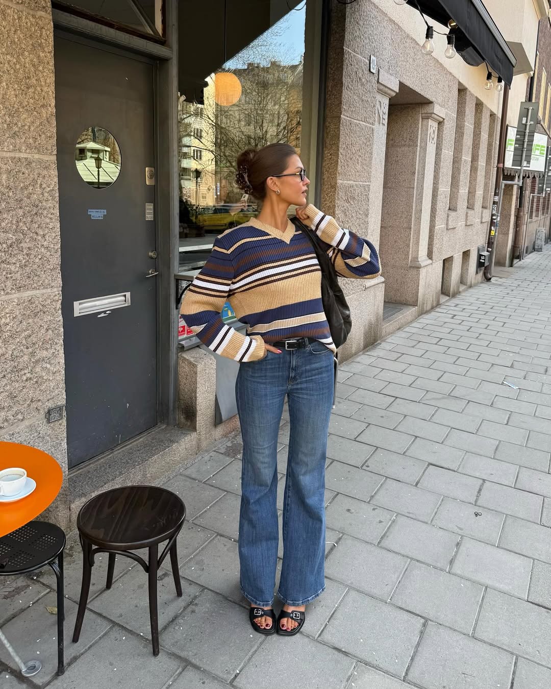 Influencer sofiaboman in a blue white beige and burgundy striped, blue flared jeans flat shoes and a black belt.