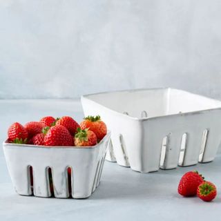 White, distressed ceramic berry carriers, one empty and one filled with strawberries