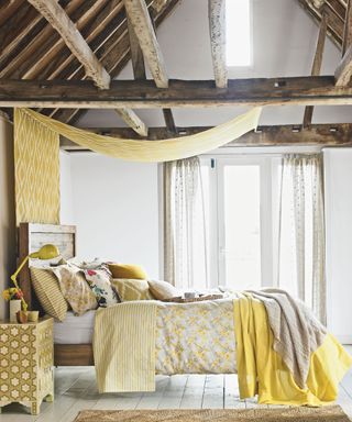 Bedroom, oak beams timber frame, rustic bed, assorted cushions and pillows, floral quilt. French windows, diamond pattern canopy