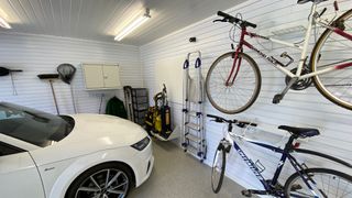 A garage with a parked car and racks for bicycles and tools