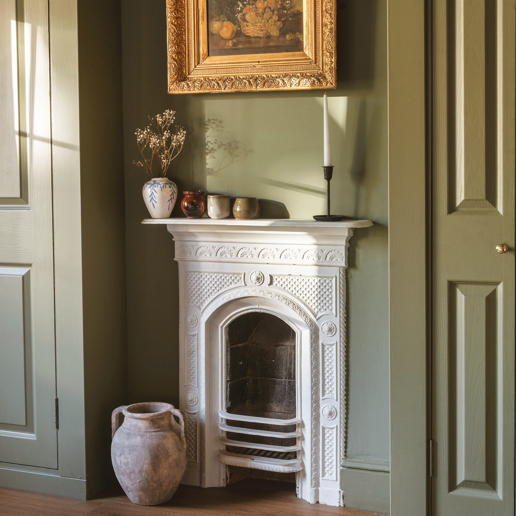 a bedroom with green walls and fitted wardrobes with a white painted traditional iron fireplace