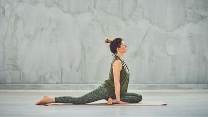 Woman doing pigeon stretch on yoga mat in stone studio looking peaceful