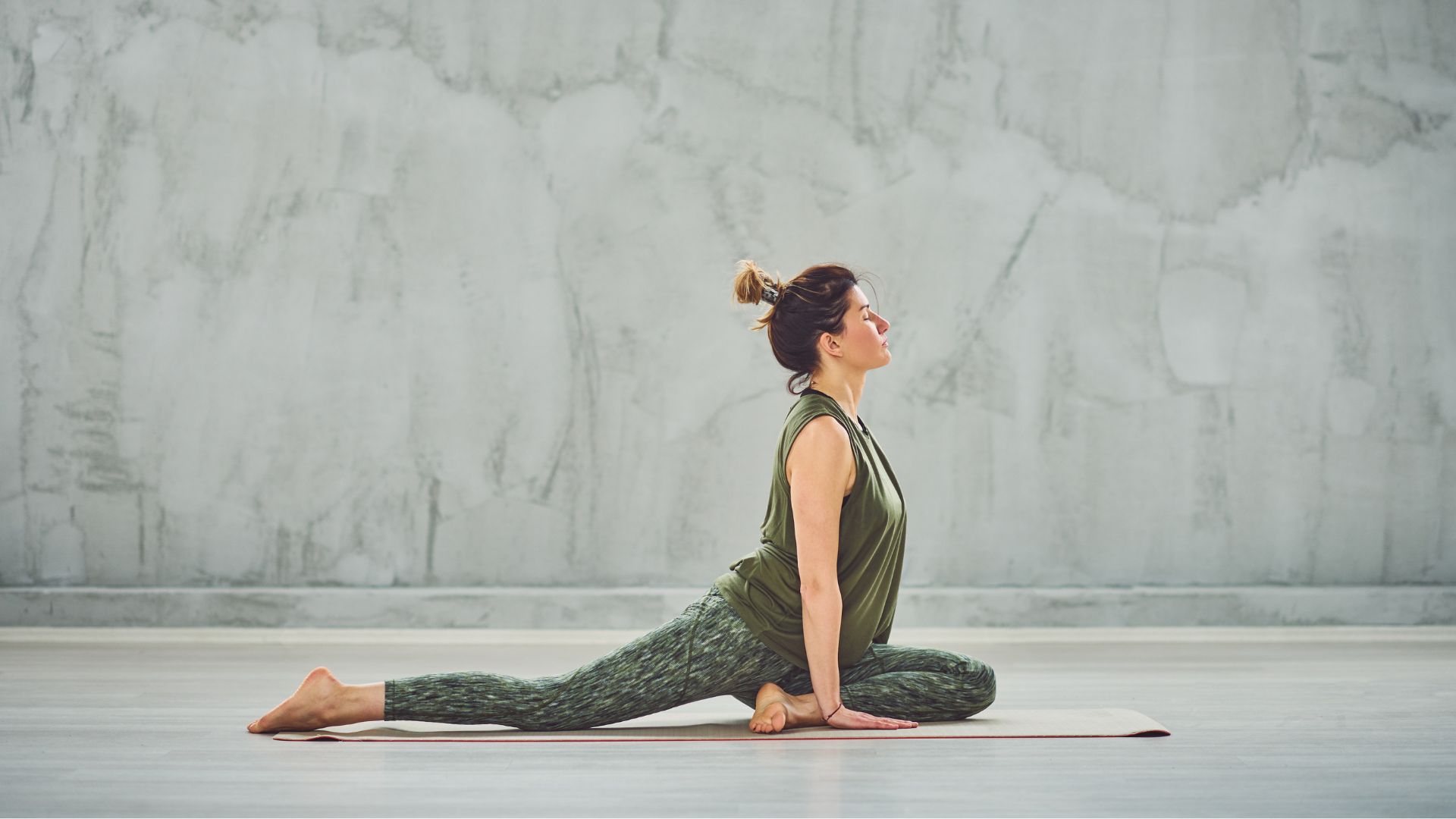 Woman doing pigeon stretch on yoga mat in stone studio looking peaceful