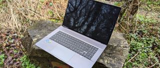 A silver MSI Creator Z17 sitting on a stone bench in a forest setting