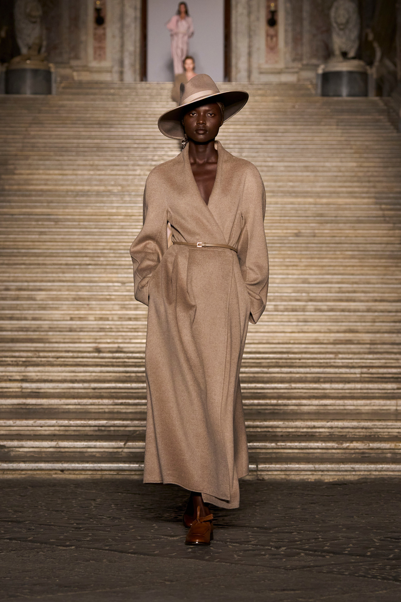 A woman wears a tan hat, and tan wrap coat.