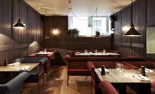 The Flying Elk, Stockholm, Sweden. A restaurant with wooden tables, grey and burgundy chairs, wooden floors and triangular pendant lights.