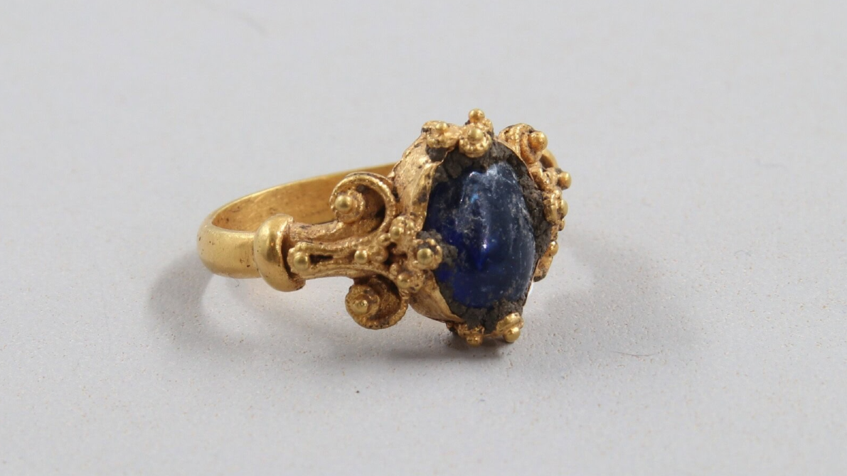 a delicately filigreed gold ring with a dark blue oval gemstone