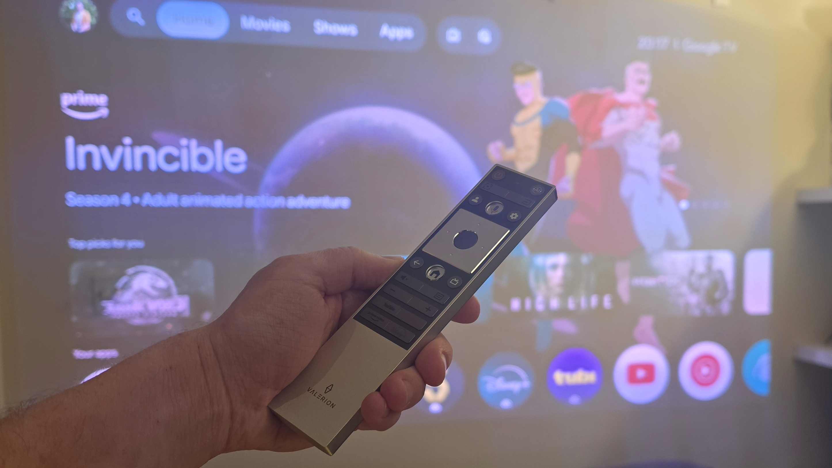 The Valerion VisionMaster 2 Pro's remote, held in front of the projected screen showing Invincible.