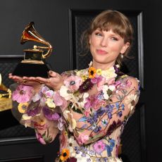 Taylor Swift wearing a flower dress and holding a Grammy award