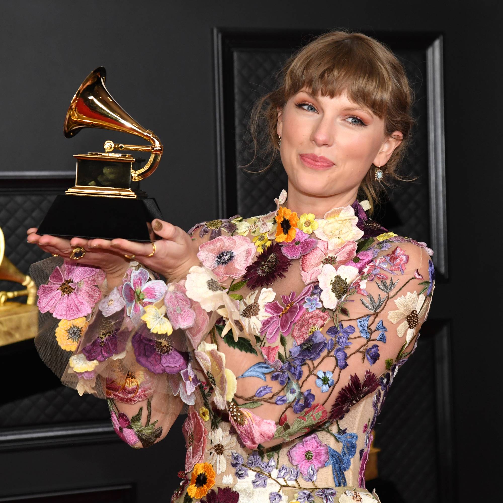 Taylor Swift wearing a flower dress and holding a Grammy award
