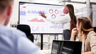 Femal eteach presenting bargraph data on a digital whiteboard in a classroom