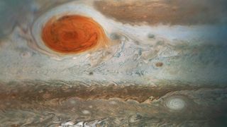 a section of swirling world of gases of tans and browns and off whites with a giant storm of blood orange swirling in the top left.