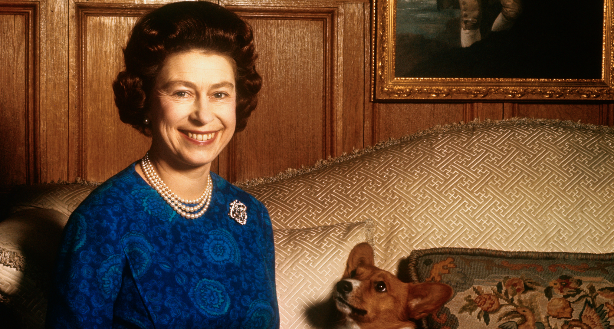 Queen Elizabeth wearing a blue dress sitting with a corgi
