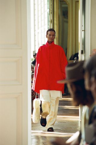 Model The Row mengenakan jaket anorak merah dengan celana krem.