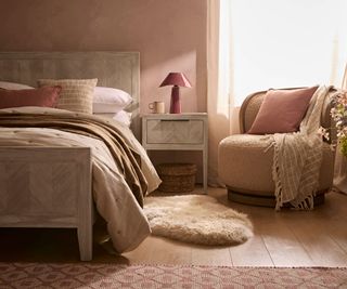 pink bedroom with wooden flooring and sheepskin rug with wooden bed and boucle armchair