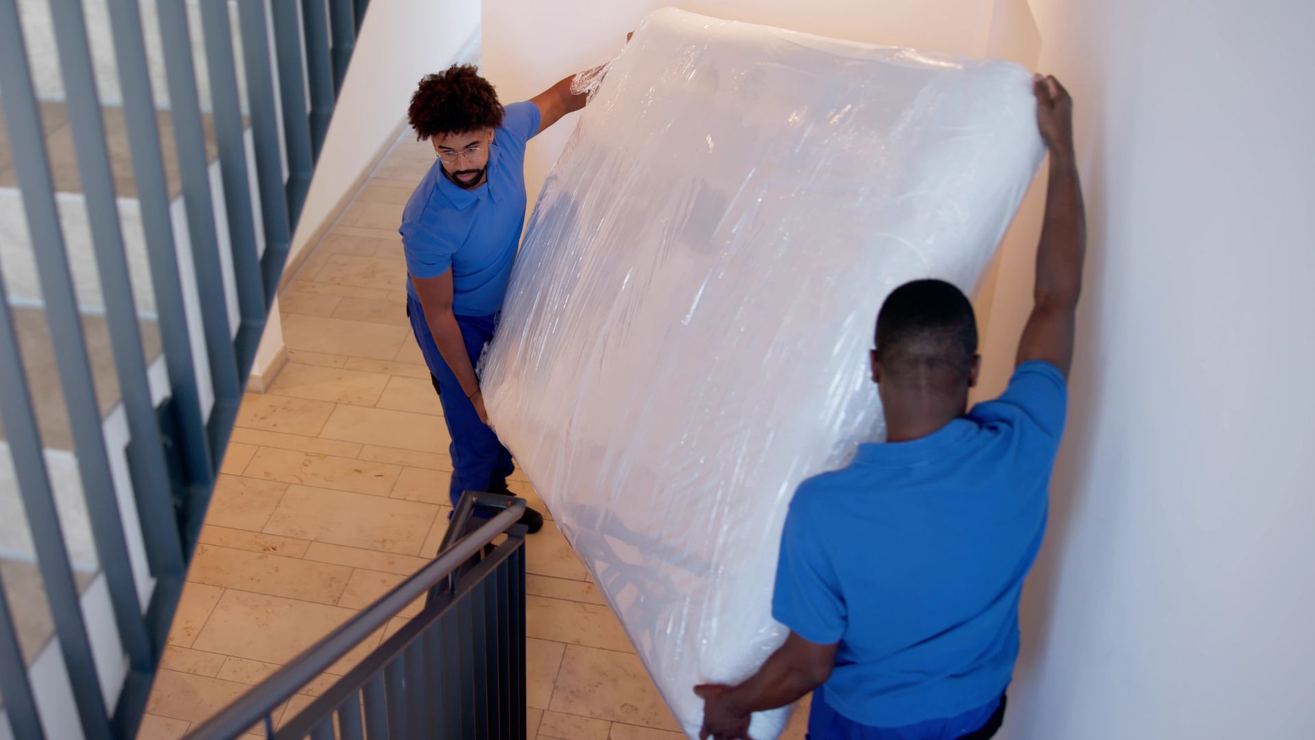 Two men carry a mattress down a flight of stairs