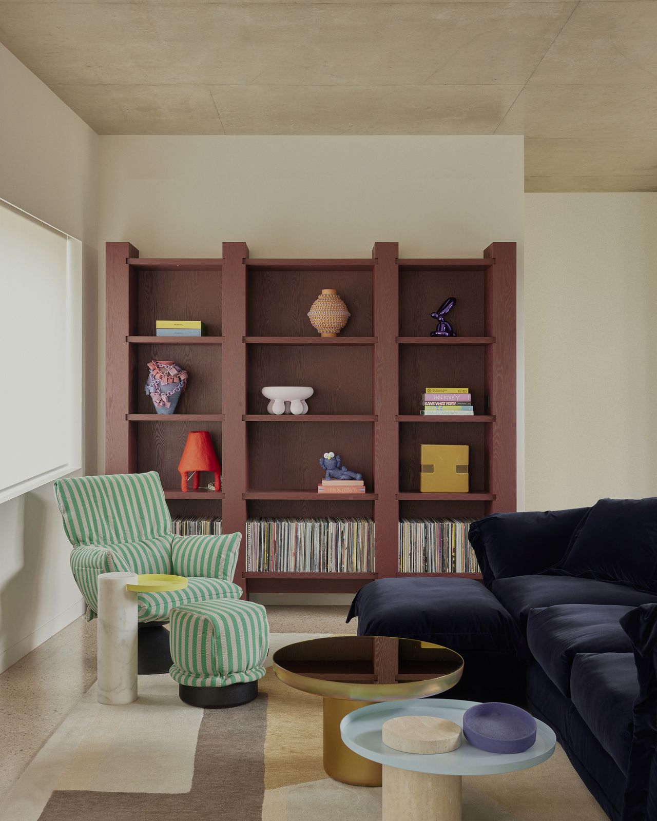colorful living room with green striped armchair and ottoman with navy blue sofa, nesting coffee table, and painted shelving unit with records and sculptures displayed on it