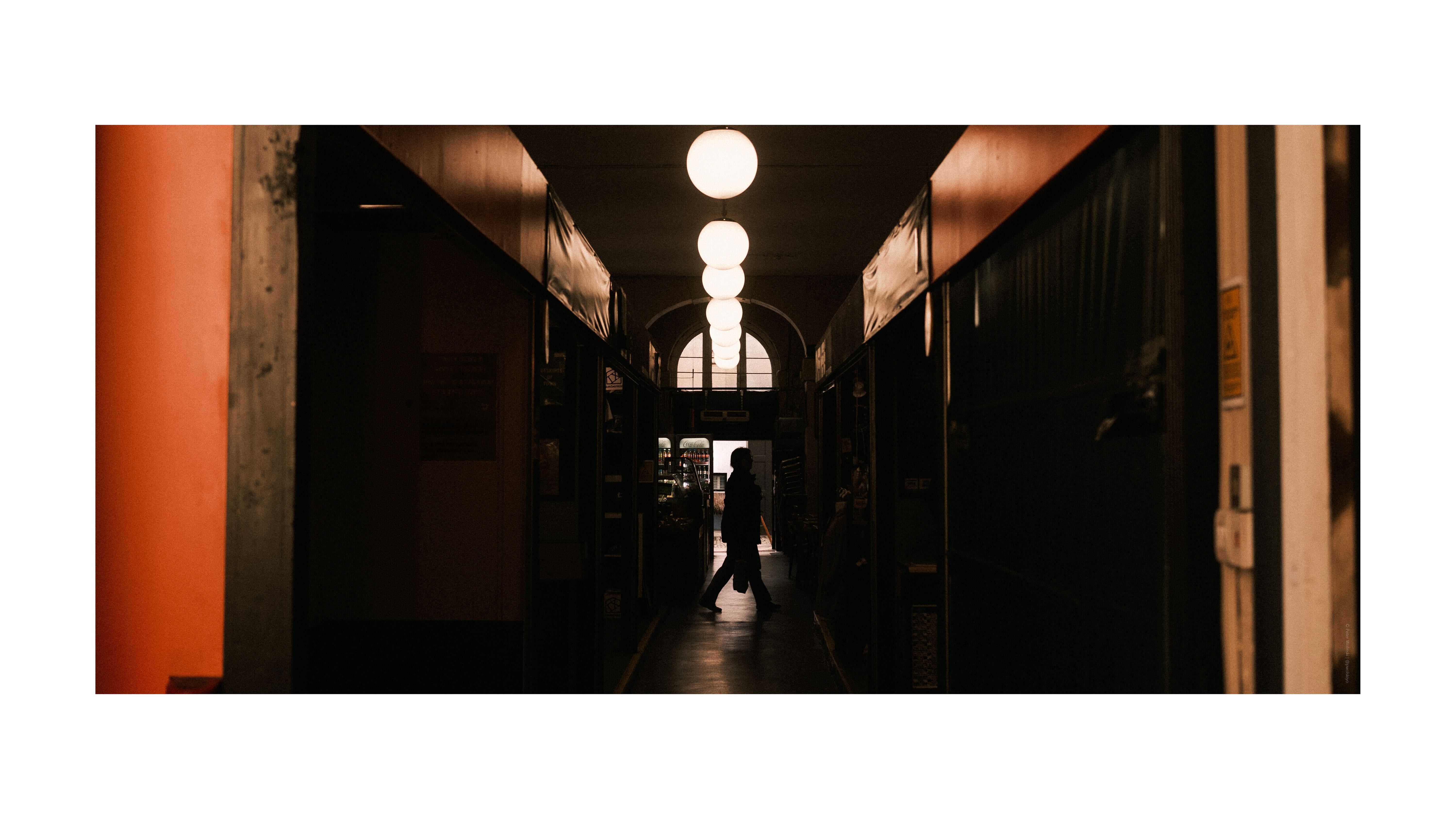 A photo of a person walking from the far end of a corridor, silhouetted against a light source.