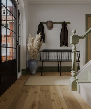 hallway with light wooden floor, white walls, black framed glass door, pale green staircase and skirting