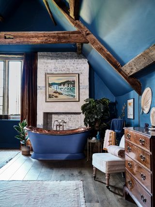 A dark blue bathroom with exposed wooden beams and a freestanding bath