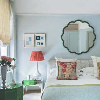 A bedroom with a scalloped mirror above the bed and a patterned table lamp