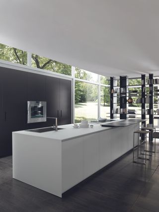 Sleeky, modern kitchen with a white kitchen island and dark wooden floors and cabinets which are one with the wall.