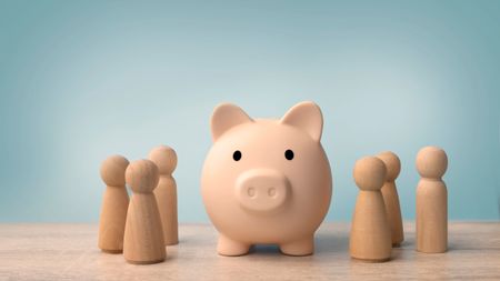 Wooden figures standing around piggy bank