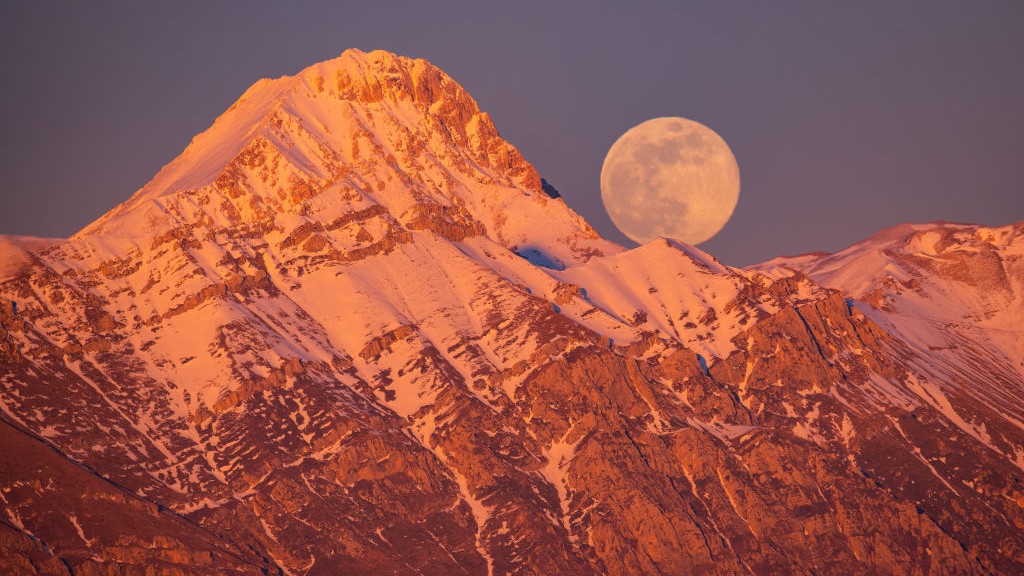 Wolf moon rising next to Corno Grande and Pizzo Cefalone peaks in Italy.