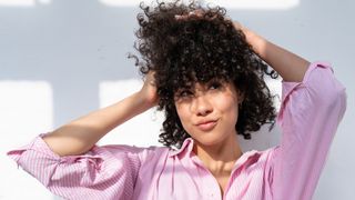 A woman in a pink shirt ruffling her curly hair