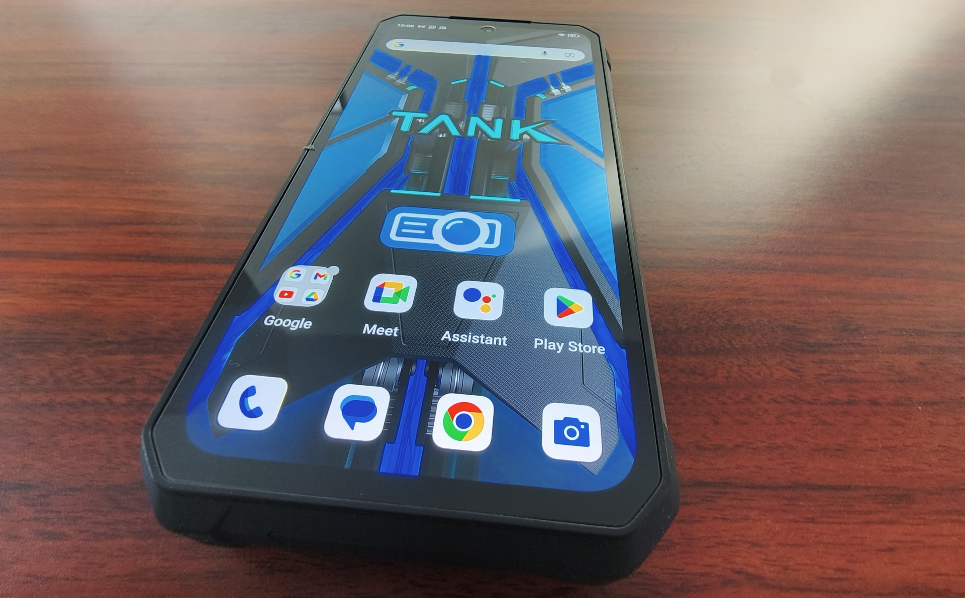 A close-up, angled view of the front of a rugged smartphone, Tank 4 Pro, displaying its home screen with app icons for Google, Meet, Assistant, Play Store, and the camera.