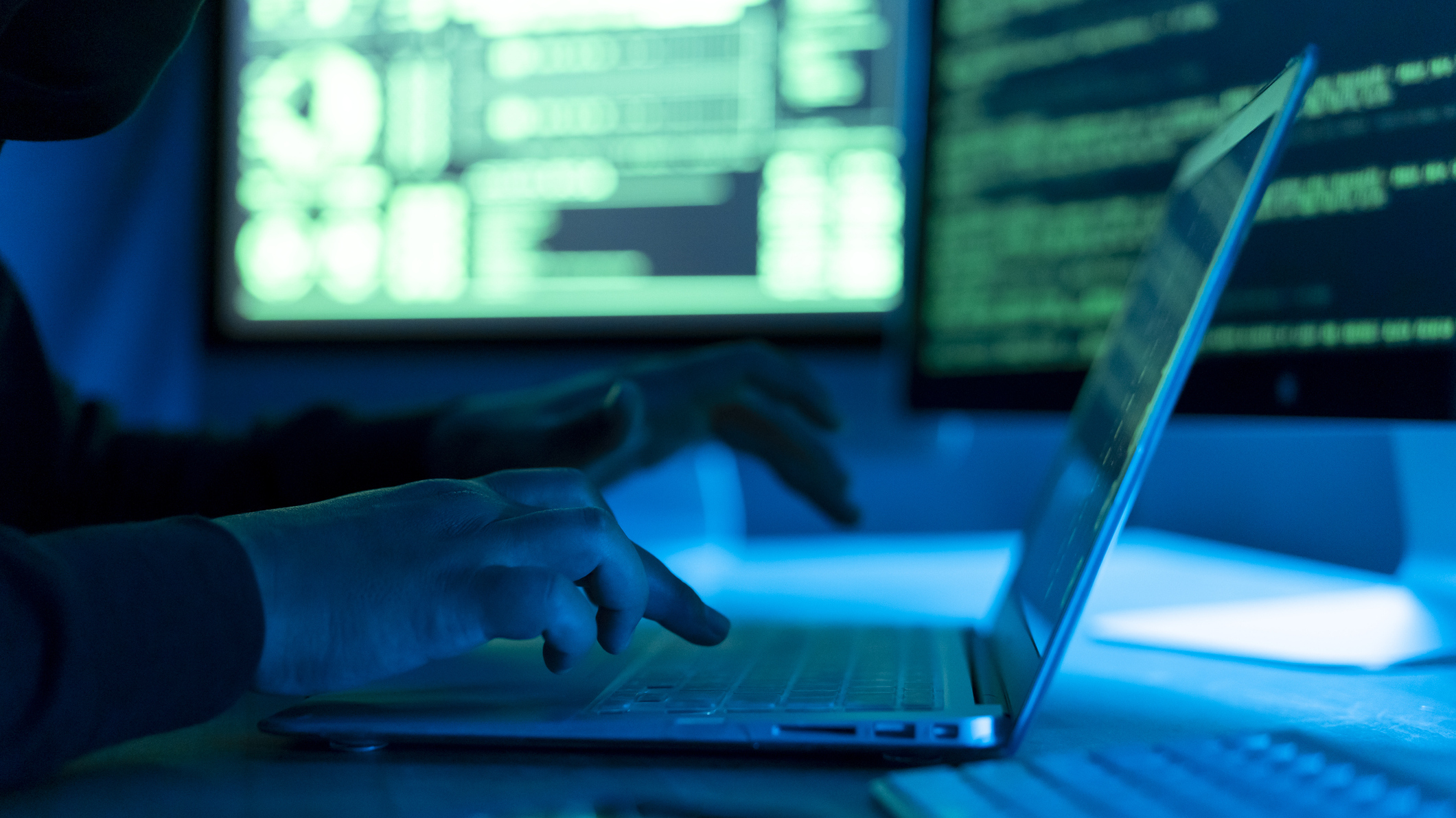 Person typing at a laptop in a darkened room, looking at an external monitor